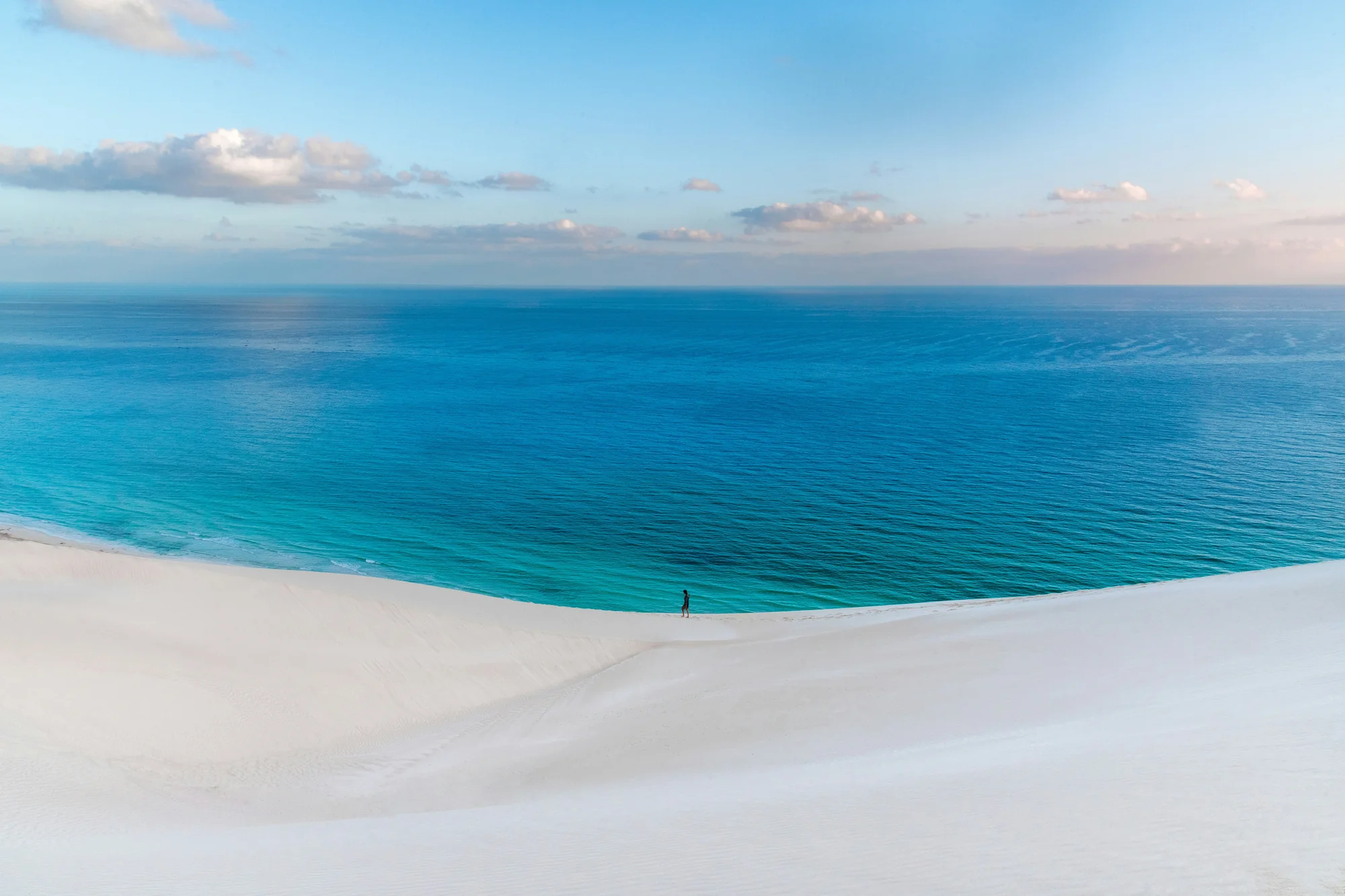 A lone traveller crossing the white dunes above the turquoise sea at Arher