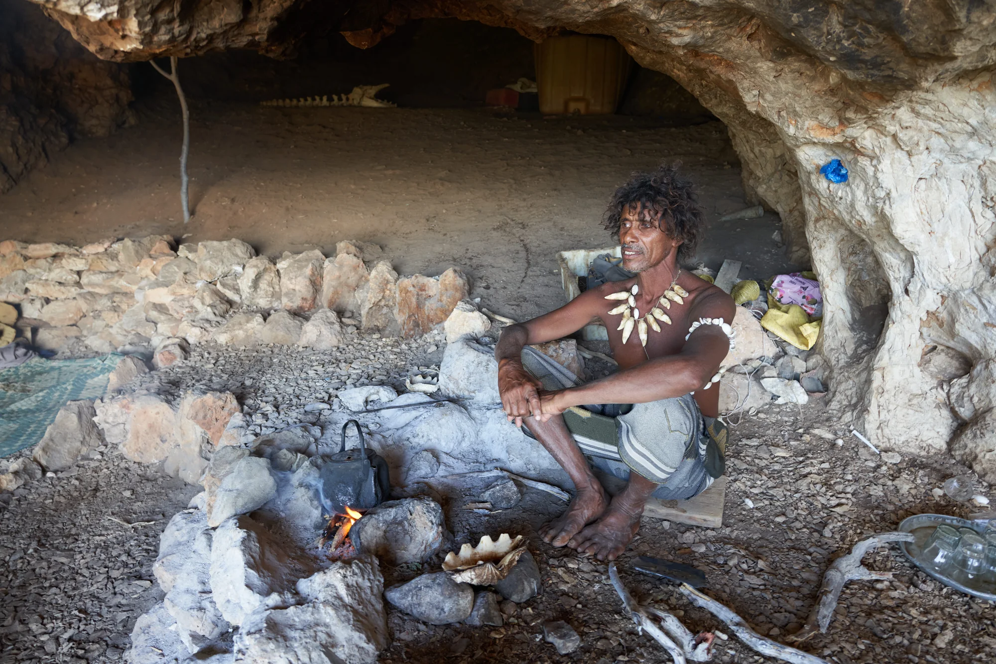 A Socotri man seated beside a small fire inside a coastal cave shelter